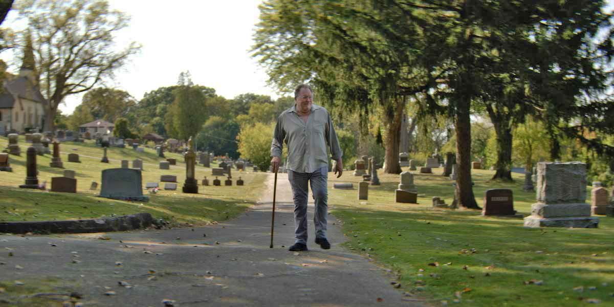 Kevin Matthews walking through a cemetery with a cane