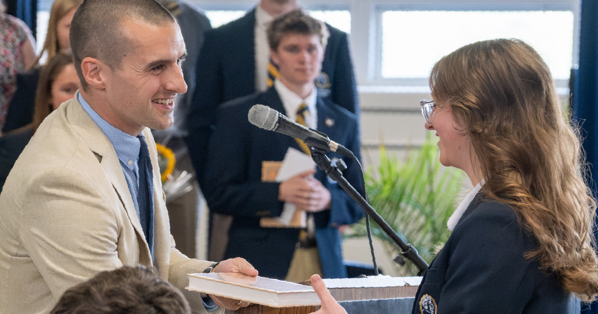 Dr. Eric DeMeuse speaks with a Chesterton Academy student at a microphone