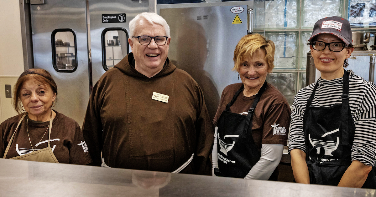 A friar and three people behind the counter at the Capuchin Soup Kitchen.